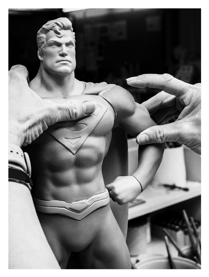Primer plano de un artesano pintando el emblema del pecho de la figura de Superman con pinceladas precisas.