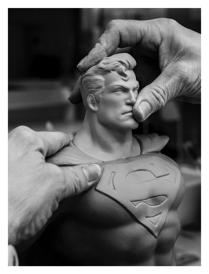 Manos ensamblando piezas de porcelana de la figura de Superman, destacando el proceso de creación artesanal.